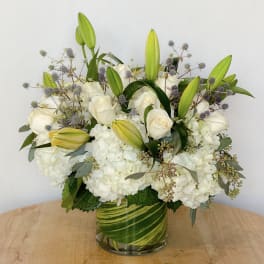 White roses and lilies arranged in a glass vase with hydrangeas