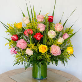 Mixed roses in pink, yellow, and red arranged in a clear glass vase
