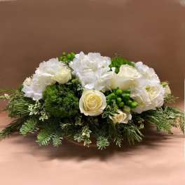 Low white floral arrangement with roses and hydrangeas on a bed of greenery
