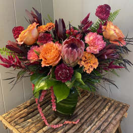 Bright mixed bouquet with orange roses and a protea in a green vase
