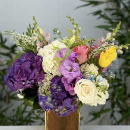 Colorful bouquet in a gold vase with purple hydrangeas, roses, and yellow tulips