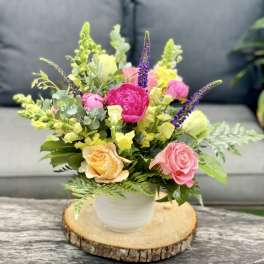 Mixed pink, yellow, and purple flowers in a white pot