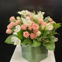 Pink roses and white alstroemeria arranged in a green glass vase