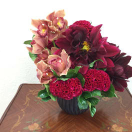 Deep red and peach floral arrangement in a black vase