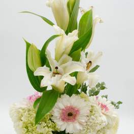 White lilies and pale flowers arranged in a clear glass vase
