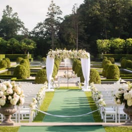 Outdoor wedding aisle with white chairs and floral arch