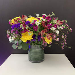 Mixed bouquet of yellow, pink, purple, and white flowers in a glass vase