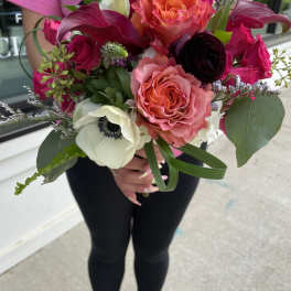 Handheld bouquet of pink, coral, and white flowers