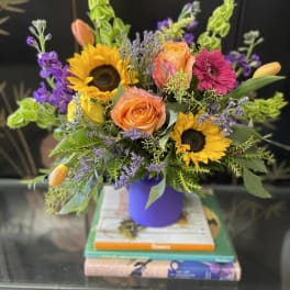 Colorful bouquet with sunflowers, orange roses, and purple flowers in a purple vase