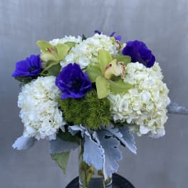 White hydrangeas with purple anemones and green orchids in a glass vase
