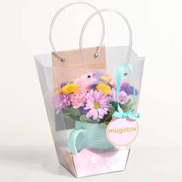 Pastel flower arrangement in a mint watering can inside a clear gift bag