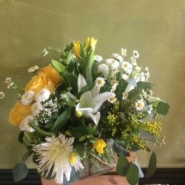Yellow and white mixed bouquet in a glass vase with a wooden crate