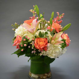 Peach roses and lilies arranged with white hydrangeas in a glass vase