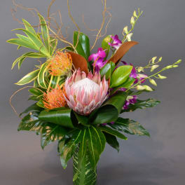 Tropical flower arrangement in a glass vase with pink protea and purple orchids