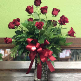 Arrangement of long-stemmed red roses in a clear glass vase with a large red bow.