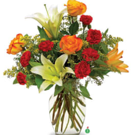 Tall bouquet of orange roses, red carnations, and white lilies in a clear glass vase