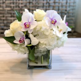 White hydrangeas and pale orchids in a square glass vase
