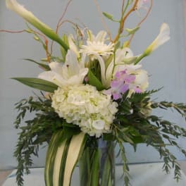 Tall white floral arrangement in a glass vase with orchids and lilies