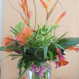 Tropical flower arrangement in a clear glass vase with orange bird-of-paradise and pink calla lilies