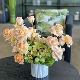Peach roses and green orchids in a white vase
