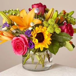 Mixed bouquet of roses, lilies, and a sunflower in a glass vase