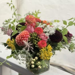 Mixed bouquet of pink, coral, yellow, and dark flowers in a glass vase