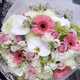 Handheld bouquet of pink gerberas, white orchids, and roses wrapped in white paper