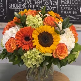 Bouquet of sunflowers, orange roses, and white hydrangeas in a glass vase