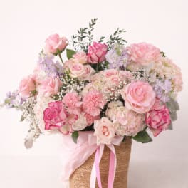 Pink and cream rose bouquet in a woven basket with ribbon