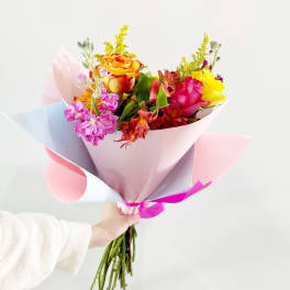 Handheld bouquet of multicolored roses and mixed blooms in pastel wrap