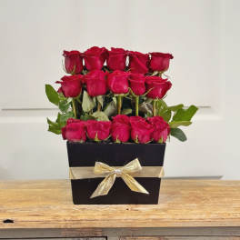 Red roses arranged in a black box with a gold ribbon