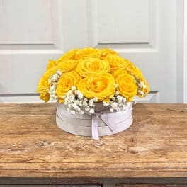 Round white box of yellow roses with small white filler flowers on a wooden table