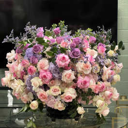 Large arrangement of pink, lavender, and cream roses in a black vase