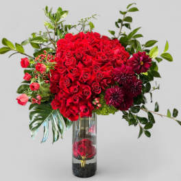 Red roses and burgundy flowers in a tall glass vase