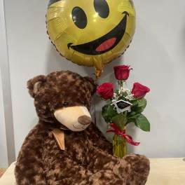 Teddy bear with a smiley-face balloon and a small rose bouquet