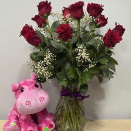 Red roses in a glass vase beside a pink plush hippo