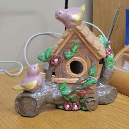 Decorative birdhouse figurine with two pink birds on a wooden table