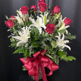 Bouquet of red roses and white lilies with a pink ribbon in a vase