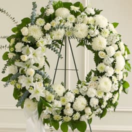 White floral wreath on a black easel with green foliage