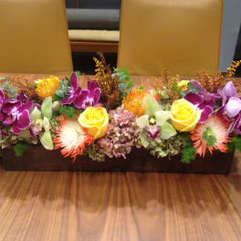 Long rectangular floral centerpiece with purple orchids and yellow roses