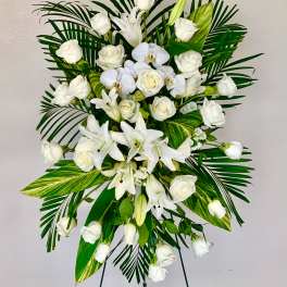 White roses and lilies arranged with palm leaves on a standing easel