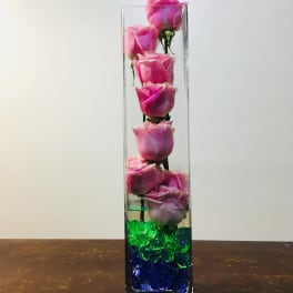 Pink roses in a tall clear glass vase with blue and green stones