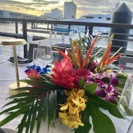 Tropical floral centerpiece with orchids, roses, and bright red blooms