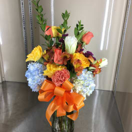 Colorful mixed flower arrangement in a glass vase with an orange bow