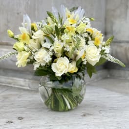 White and yellow floral arrangement in a round glass vase