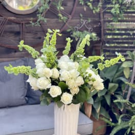 White roses and green spikes arranged in a tall vase