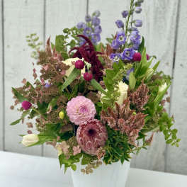 Mixed bouquet of pink, purple, and cream flowers in a white vase