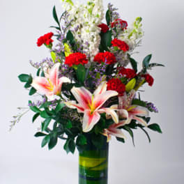 Tall bouquet of lilies and red carnations in a glass vase