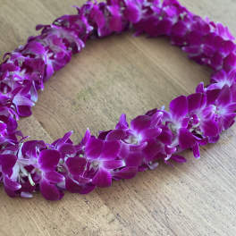 A purple orchid lei laid in a loop on a wooden surface.