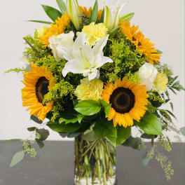 Bouquet of sunflowers, white lilies, and yellow carnations in a glass vase
